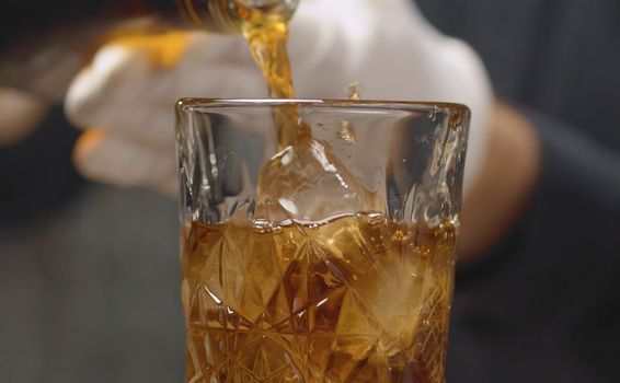 Making a Long Island Ice Tea Cocktail. Close up bartenders hands pouring cold tea into a crystal glass with ice.