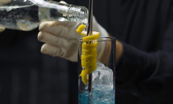 Preparing of Blue Lagoon Cocktail. Close up bartenders hands, pouring vodka into a glass with ice cubes and blue curacao liquor