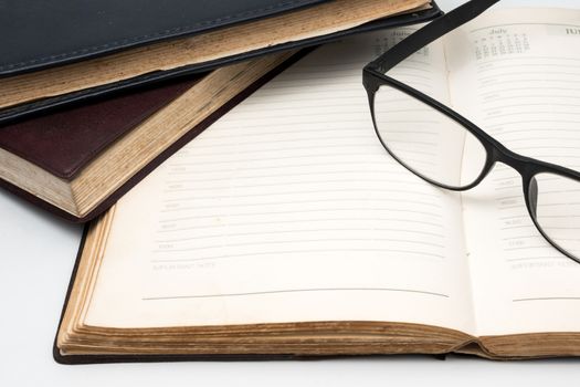 A stack of old books with notebook and eyeglasses on a white background.