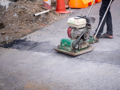 Worker use vibratory plate compactor compacting asphalt at road repair