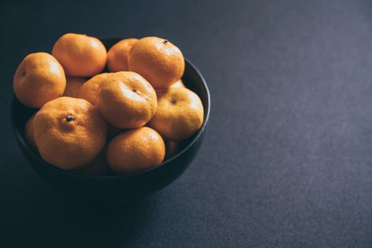 Fresh tangerines in bowl, Orange fruits on dark background.