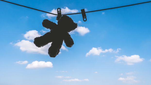 Silhouette of Teddy bear hanging on the clothes line with blue sky.