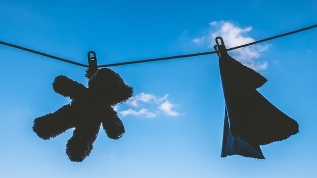 Silhouette of Teddy bear and napkin hanging on the clothes line with blue sky.