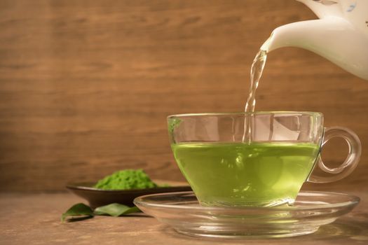 Green tea being poured into glass tea cup on the table
