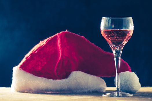 Glass of wine with Santa hat on the wooden table, black background.