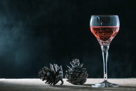 Glass of wine with pine cones on the wooden table, black background, free space for text