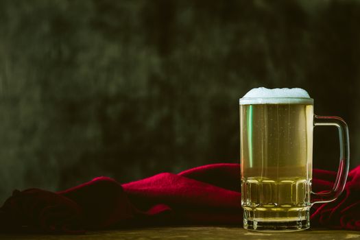 Mug of beer with red scarf on the wooden table. Free space for text