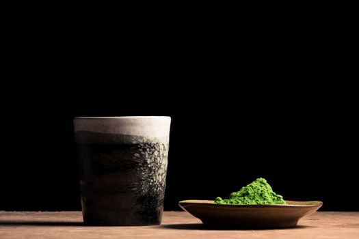 a ceramic cup and green tea powder on the table, black background. Free space for text