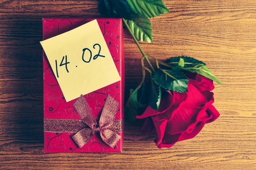 Red gift box with red rose on wooden background. Concept of Valentine Day.