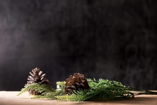 Pine cones with branches on the wooden table, black background, free space for text