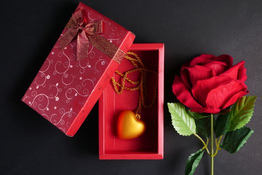 Red rose with gold heart necklace in red gift box on black background. Concept of Valentine Day.