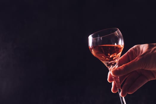 Male hand holding a glass of wine on black background. Free space for text