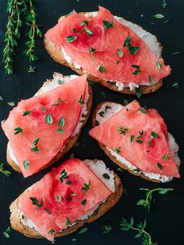 Toasts with soft cheese and watermelon.Salty cheese,sweet watermelon and spicy thyme on crispy grilled bread slices.Idea and recipe for unusual healthy breakfast,summer snack or lunch.Top view flatlay