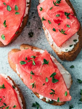 Toasts with soft cheese and watermelon.Salty cheese,sweet watermelon and spicy thyme on crispy grilled bread slices.Idea and recipe for unusual healthy breakfast,summer snack or lunch.Top view flatlay