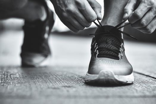 Cropped image of hands tying shoelaces on sneaker, running surface background. Hands of sportsman with pedometer tying shoelaces on sporty sneaker. Running equipment concept. Shoelaces tying by male hands.