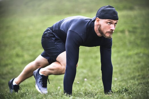 Muscular sportsman stretching out before a sports training at the street in city park