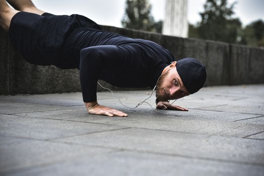 Young bearded sportsman makes workout in a park, doing a series of push ups outdoor.