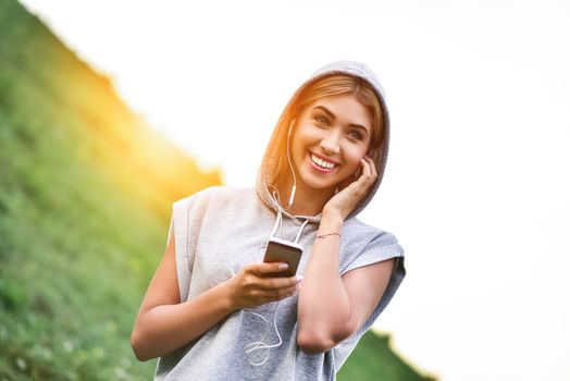 Beautiful young woman with headphones glad after nice jogging in city park