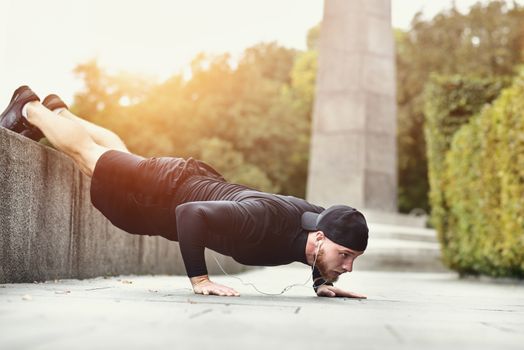 Young bearded sportsman makes workout in a park, doing a series of push ups outdoor.