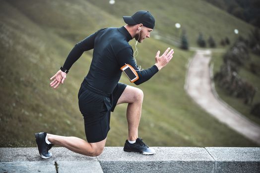 Young caucasian male jogger with fitness tracker attached to arm do warming up before jogging.