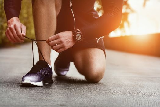 Cropped image of hands tying shoelaces on sneaker, running surface background. Hands of sportsman with pedometer tying shoelaces on sporty sneaker. Running equipment concept. Shoelaces tying by male hands.