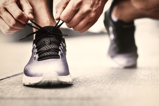 Cropped image of hands tying shoelaces on sneaker, running surface background. Hands of sportsman with pedometer tying shoelaces on sporty sneaker. Running equipment concept. Shoelaces tying by male hands.