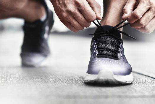 Cropped image of hands tying shoelaces on sneaker, running surface background. Hands of sportsman with pedometer tying shoelaces on sporty sneaker. Running equipment concept. Shoelaces tying by male hands.