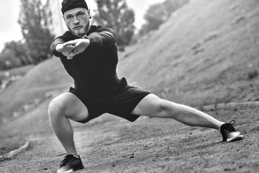 Muscular sportsman stretching out before a sports training at the street in city park