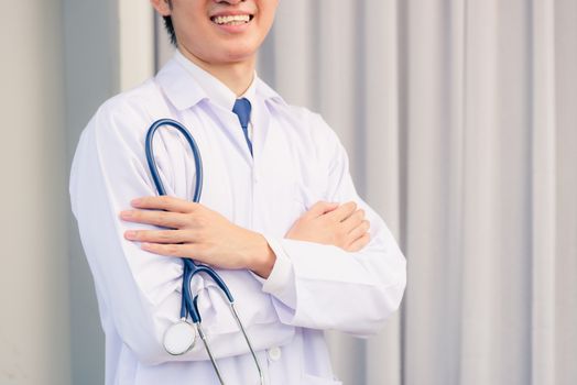 Portrait closeup of Happy Asian young doctor handsome man smiling in uniform stand crossed arm hold stethoscope on hand looking to camera with cop space, healthcare medicine concept