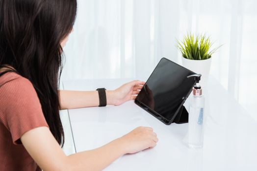 Work from home, Asian young businesswoman wearing face mas protactive video conference call or facetime touch digital smart tablet computer she meeting with colleagues on desk, situation coronavirus