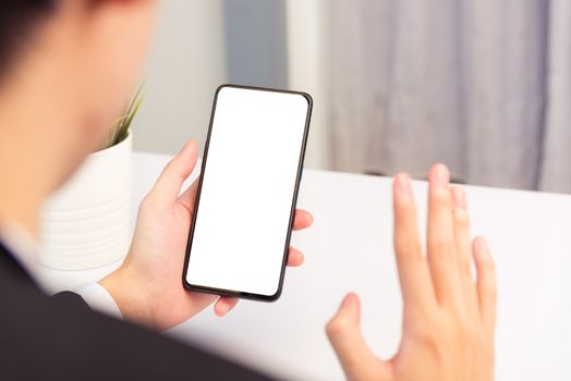 Work from home, Back view of Asian young businessman smile wearing suit video conference call or facetime by smart digital mobile phone blank screen raise hand to say hello teammates on desk