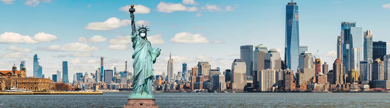 The Statue of Liberty wearing surgical mask when Covid-19 Outbreak over panorama of New york cityscape river side, united state, coronavirus pandemic, Architecture and building with tourist concept