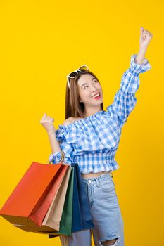 Attractive Asian smiling young woman Carrying shopping coloful bag on isolated yellow color background, copy space and studio, black friday season sale concept.