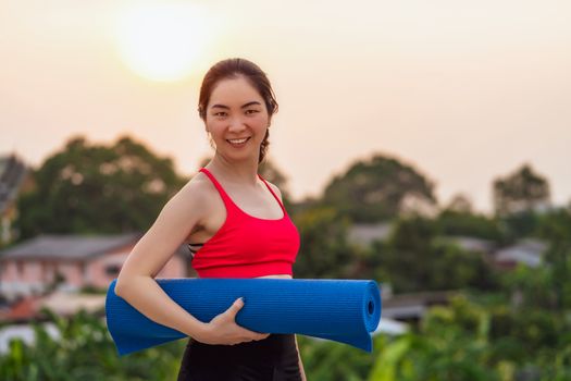 Asian woman holding yoga mat from home at rooftop when Covid19 outbreak and lockdown, healthy or Meditation Exercise, yoga workout at home, coronavirus pandemic and quarantine, sports and healthcare