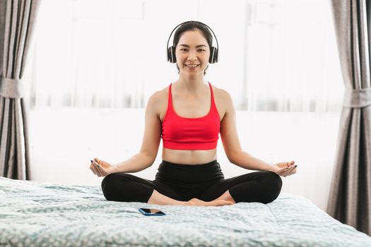 Asian woman practicing yoga from home on bed in bedroom when Covid19 outbreak, healthy or Meditation Exercise, yoga workout at home, coronavirus pandemic and quarantine, sports and healthcare concept