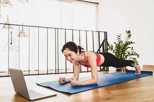 Asian woman practicing yoga from home with laptop when Covid19 outbreak and lockdown, healthy or Meditation Exercise, workout at home, coronavirus pandemic and quarantine,sports and healthcare concept