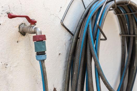 garden hose connected to a tap on a white wall with worn paint