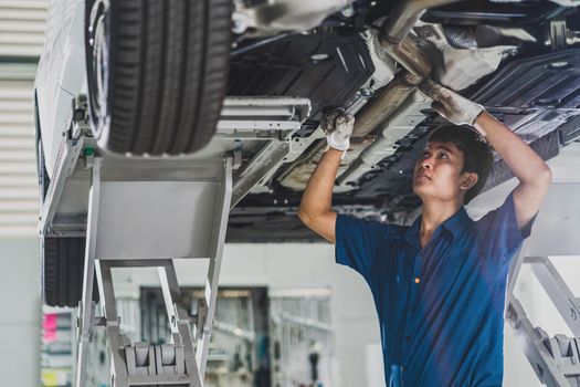 Asian mechanic repairing and light up under the car in maintainance service center which is a part of showroom, technician or engineer professional work for customer, car repair and maintain concet