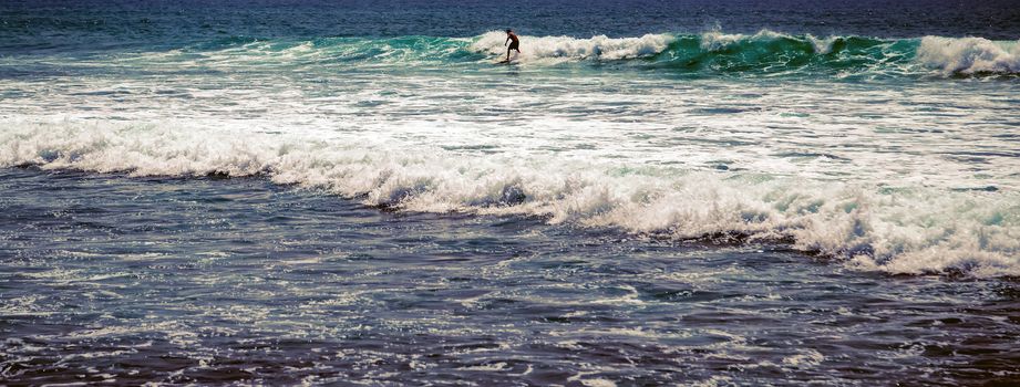 Surfer man on Blue Ocean Wave Bali Indonesia water sport lessons swimming activity riding waves