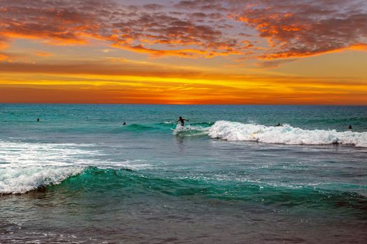 Silhouette surfer riding ocean waves in Bali Indonesia surfboard on a beach at sunset.