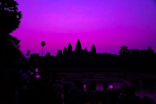Tourist taking picture smartphone Angkor Wat temple Romantic Sunrise Purple silhouette reflection on water pond background. Holy place in Asain. Popular tourist attraction ancient temple.