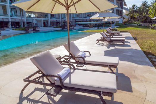 Swimming pool luxury tropical resort panoramic. Sunbathing deck sun loungers relaxing seats and sun umbrella.