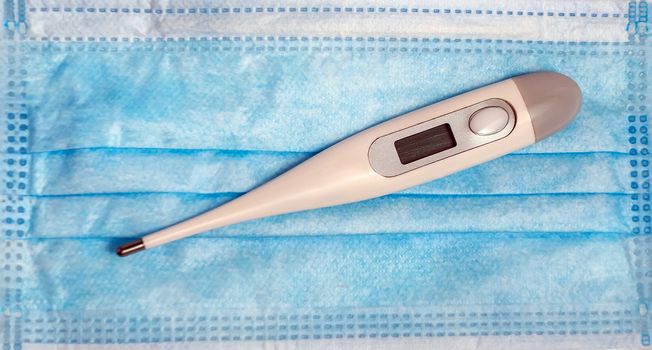 Thermometer electronic medical check in Medical mask. Safety protection respiratory face nose mouth air mask hygiene on blue background.
