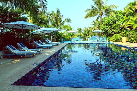 Sunbathing deck with umbrella swimming pool hotel resort beach panoramic sea view blue background. Silhouette coconut palm tree. Relaxing summer tropical resort.