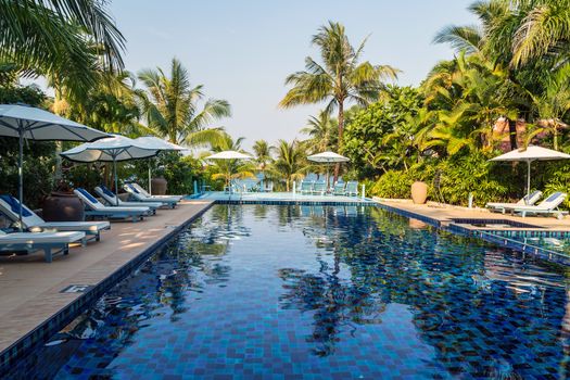 Sunbathing deck with umbrella swimming pool hotel resort beach panoramic sea view blue background. Silhouette coconut palm tree. Relaxing summer tropical resort.
