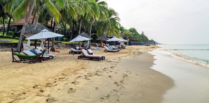 Tropical views from Long Beach Phu Quoc Island, Vietnam. Nobody on the beach. Palm tree white umbrella and sun chairs in background. Eco tourism.