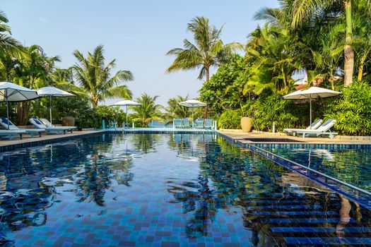 Sunbathing deck with umbrella swimming pool hotel resort beach panoramic sea view blue background. Silhouette coconut palm tree. Relaxing summer tropical resort.