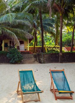 Rest sand beach with beach chairs. Maldives island, white sandy beach and sea. Luxury beach resort or hotel, beach villas and two sun chairs with sun umbrella under palm trees on white sand.