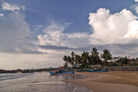 Colorful fishing boats on a long sandy beach on the ocean coast of Sri Lanka. Popular landmark fishing