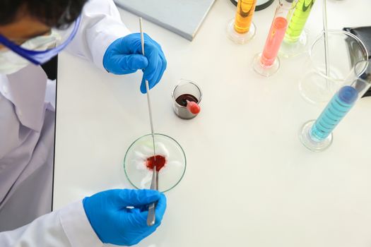 Asian professional doctor scientist wearing glasses and blue rubber gloves using needle and forceps to research in working laboratory with glassware.  Science and Healthcare, Coronavirus (Covid-19) Protection Concept.